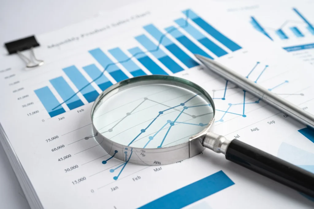 Lupa sobre gráficos financieros representando la auditoría y el informe del experto externo en prevención de blanqueo.